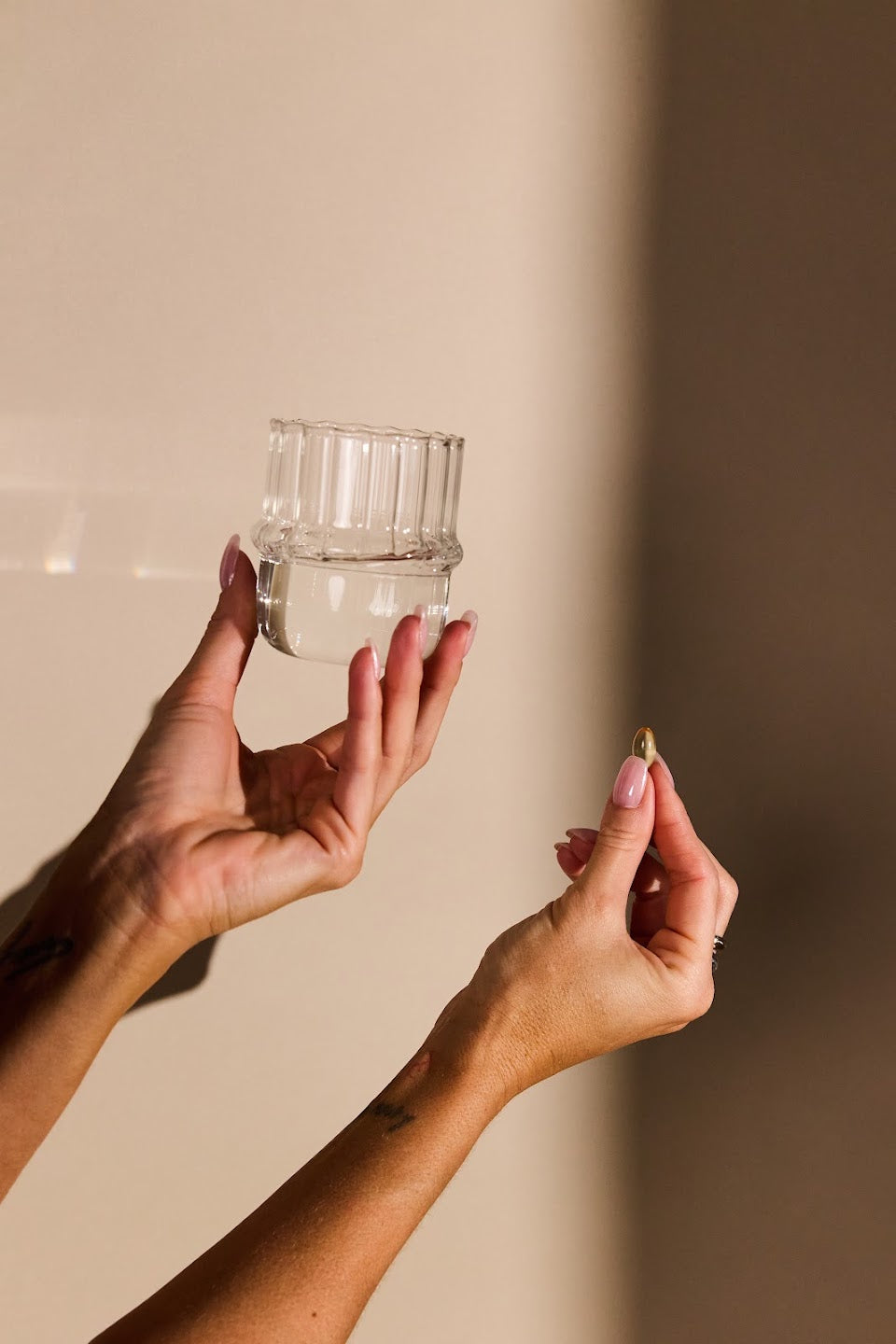 Handen met een glas water en een Algae Omega capsule in warm zonlicht