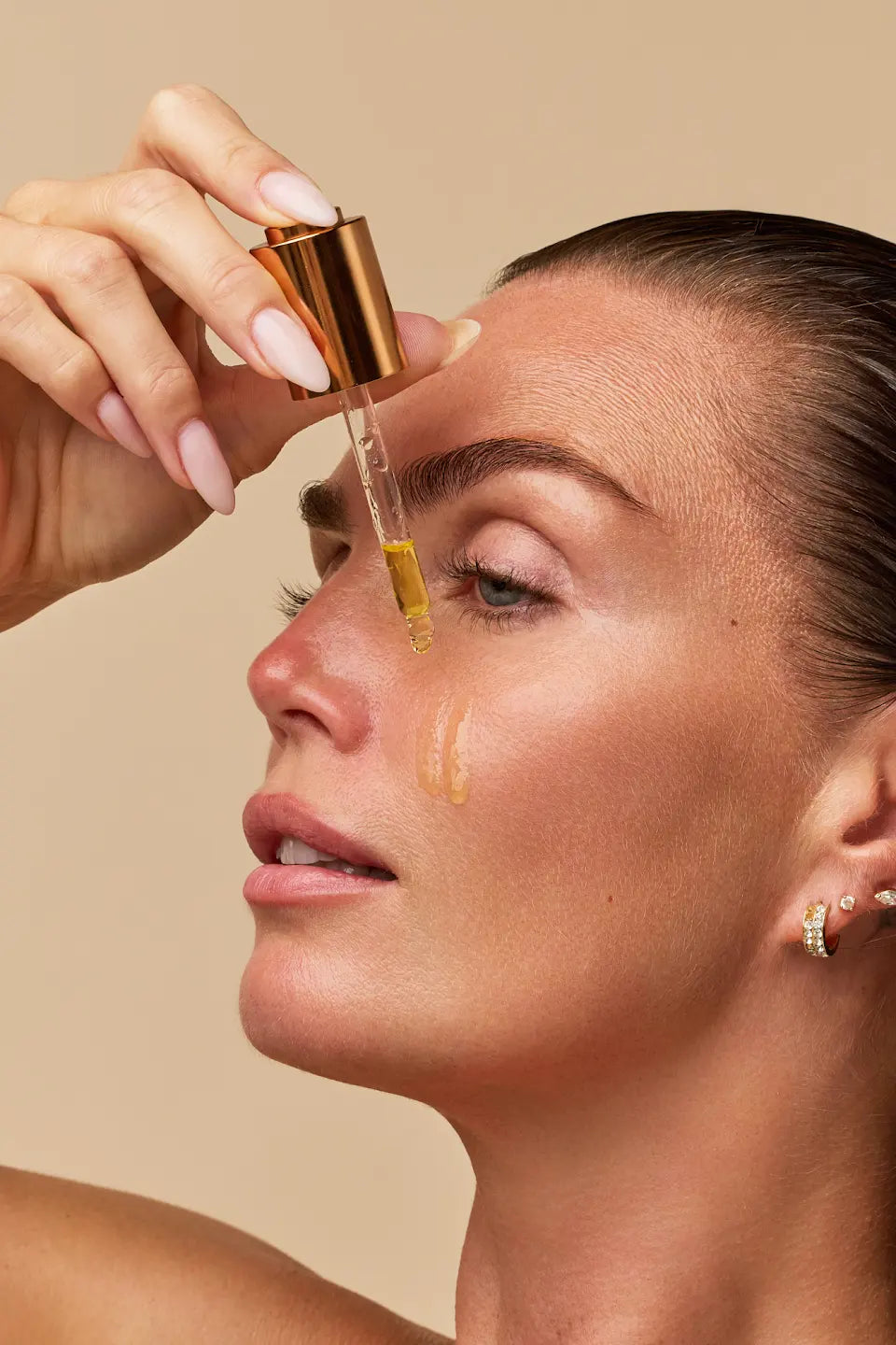 Kim brengt Glow Up Face Oil met een pipet aan op haar huid.